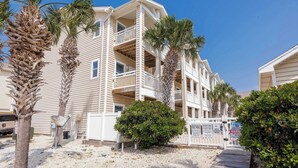 A multi-story hotel with balconies, palm trees, and a sandy ground.