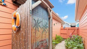 A wooden fence with a lifebuoy attached, a bamboo fence with a colorful mural, and a pathway with green plants. - Delightful Stays 2 Bdr | Pool | | Sleeps 8 (Port Aransas)