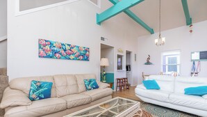 A living room with a beige sofa, a white sofa, and a glass coffee table. There is a colorful painting on the wall and a chandelier. - Private Pool | Pets | Sleeps 7 | Long Term Stays (Port Aransas)