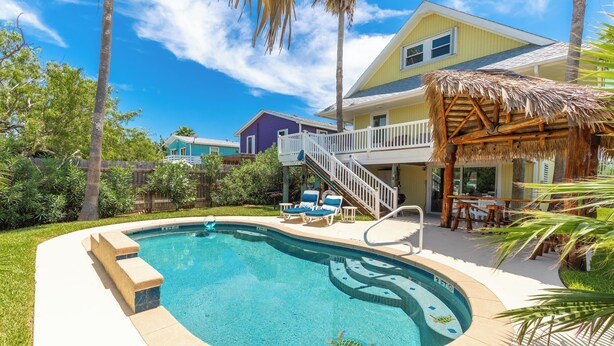 A swimming pool with a thatched roof structure, a covered deck, and a staircase leading to a second-story balcony. - Private Pool | Pets | Sleeps 7 | Long Term Stays (Port Aransas)