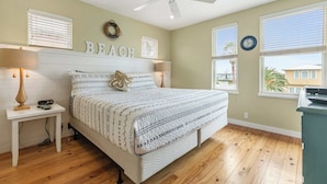 A bedroom with a bed, a ceiling fan, a nightstand, a lamp, and a wall clock. - Prime Location 5 Bedrooms | Pool | Sleeps 12 (Port Aransas)