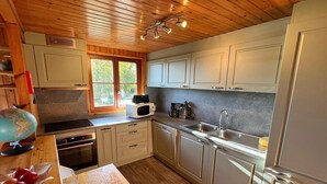 Ett modernt kök med träpanel i taket, vita skåp, rostfria vitvaror och ett fönster som släpper in naturligt ljus.
