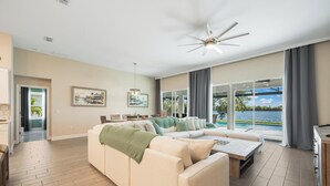 Een moderne woonkamer met een beige modulaire bank, een salontafel en uitzicht op een waterlichaam door grote ramen.