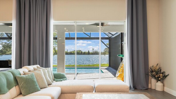 Een moderne woonkamer met een grote hoekbank, een bijzettafeltje en uitzicht op een zwembad en groen.