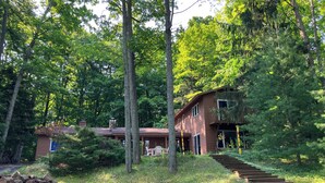 Une cabane dotée d’une terrasse en bois, entourée de grands arbres et d’une structure en pierre.