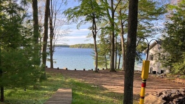Un sentier en bois mène à une propriété au bord du lac, où se trouvent une maison et une pile de bûches.