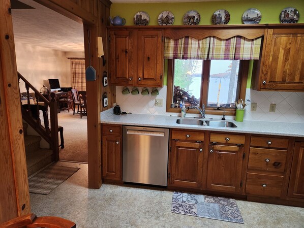 A kitchen with wooden cabinets, a stainless steel dishwasher, and a window with a plaid curtain.