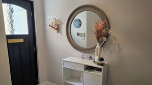 Een gang met een zwarte deur, een witte console tafel, een spiegel, een kleine potplant en een decoratief object.