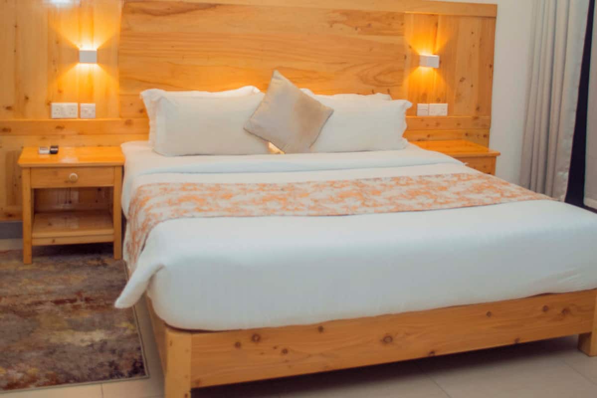Ein Schlafzimmer mit einem Holzbettrahmen, weißer Bettwäsche, zwei Nachttischen mit Lampen und einem großen Fenster mit Vorhängen.