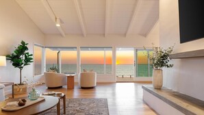 A modern living room with a large window overlooking the sea, a fireplace, and a cozy seating area. - Oceanfront Luxury with Pool/Spa, Beach Access (Encinitas)