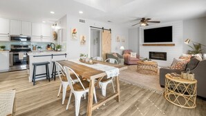 A modern kitchen with white cabinets, a wooden dining table, and a ceiling fan.