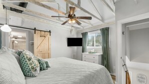 A bedroom with a bed, a ceiling fan, a TV, and a sliding barn door.