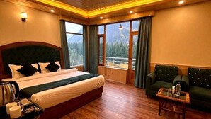 Camera d'albergo con un letto grande, una poltrona, un tavolino e vista sulle montagne.
