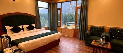 Habitación de hotel con una cama grande, un sofá, una mesita de café y vistas a las montañas.