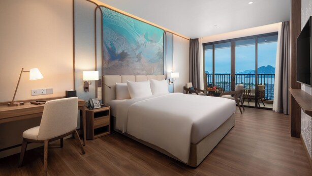 Camera d'albergo con un letto grande, una scrivania con una sedia, una TV e un balcone con vista sul mare.