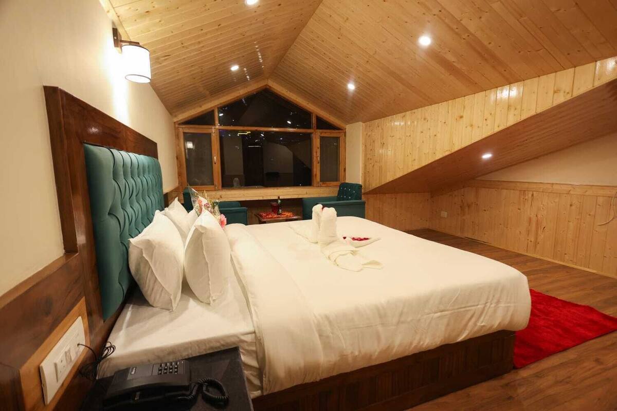 Habitación de hotel con techo de madera, una cama grande con ropa blanca, una alfombra roja y un cabecero de madera.