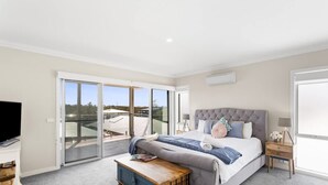 A bedroom with a large bed, a TV, a bedside table, a lamp, and a sliding glass door leading to an outdoor area. - Coastal Family Retreat in CW (Cape Woolamai)