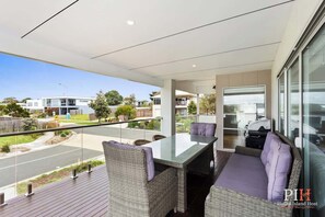 Enjoy the serene views of the surrounding neighborhood from this spacious balcony with a glass railing, glass table, and comfortable seating area.