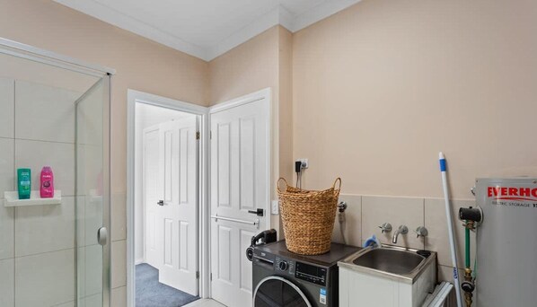 A bathroom with a washing machine, a sink, a basket, and toiletries on a shelf. - Stunning Ocean Views San Remo (San Remo)