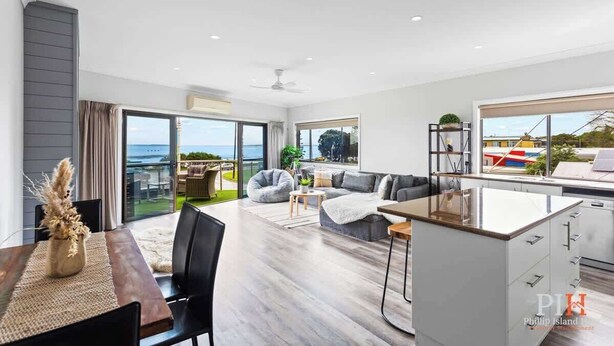 A modern living room with a dining area, a kitchen, and a large sliding glass door leading to a balcony with a view of the sea. - Stunning Ocean Views San Remo (San Remo)
