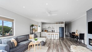 A modern kitchen with white cabinets, a central island, and a dining area with a table and chairs. - Stunning Ocean Views San Remo (San Remo)