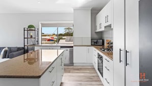 A modern kitchen with white cabinetry, a granite countertop, and a built-in dishwasher. - Stunning Ocean Views San Remo (San Remo)