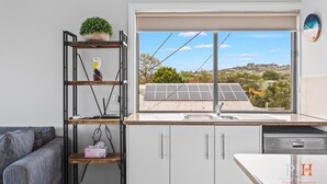 A modern kitchen with a large window, a built-in shelf with a plant, and a view of solar panels. - Stunning Ocean Views San Remo (San Remo)