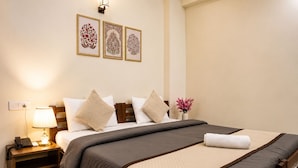 A neatly made bed with a dark and light grey bedspread, a wooden headboard, and a bedside table with a lamp and phone. - Anandmaya Retreat Tapovan Rishikesh (Rishikesh)