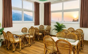 Un comedor con mobiliario de mimbre, ventanas amplias con cortinas y vista a un atardecer.