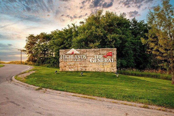A stone sign with "Highlands Restaurant" and "The General Golf Course" written on it, surrounded by greenery.