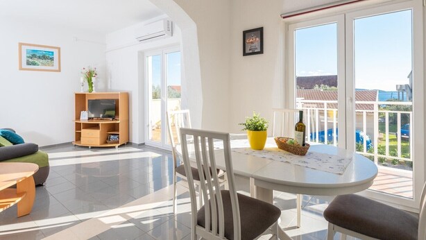 A bright living room with a TV, sofa, and dining area with a table and chairs. - Beautiful 2-Bedroom Apartment with Balcony and Sea View. (Orebic)