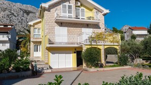 A two-story building with a yellow facade, white shutters, and a balcony with a white railing. - Beautiful 2-Bedroom Apartment with Balcony and Sea View. (Orebic)