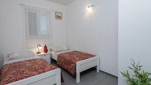 A bedroom with two single beds, a nightstand with a lamp, a window with sheer curtains, and a wall-mounted light fixture. - Beautiful 2-Bedroom Apartment with Balcony and Sea View. (Orebic)