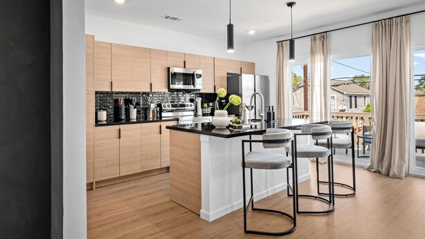 A modern kitchen with wooden cabinets, a black countertop, and a central island with bar stools.