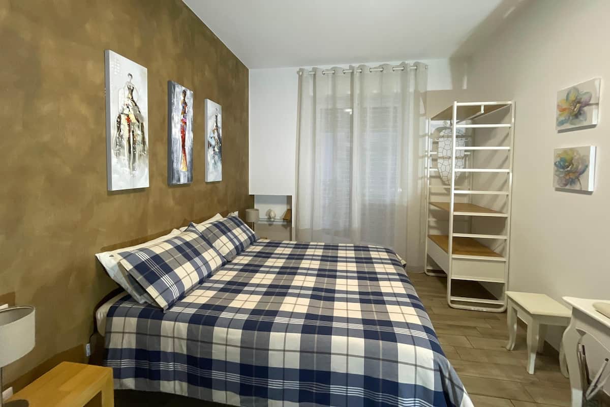 Quarto com cama, mesa de cabeceira, luminária, guarda-roupa e obras de arte nas paredes.