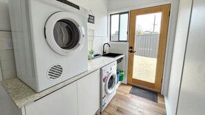 A compact laundry room with a front-loading washing machine, a smaller front-loading dryer, and a sink with a window above it. - Casa Del Batson - Your home away from home (Robe)