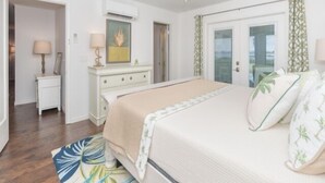 A bedroom with a bed, a dresser, a nightstand, an air conditioning unit, a ceiling fan, and a door with a view.