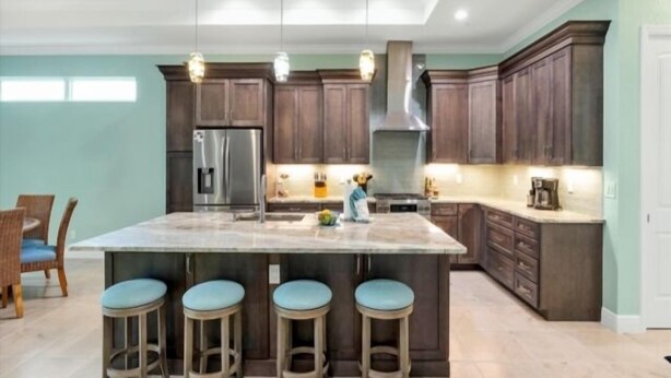 A kitchen with a large island, bar stools, a refrigerator, and wooden cabinets.