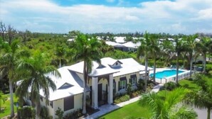 A large house with a swimming pool, surrounded by palm trees and greenery.