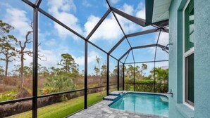 A covered outdoor area with a swimming pool, surrounded by a metal fence, and a view of the natural landscape.