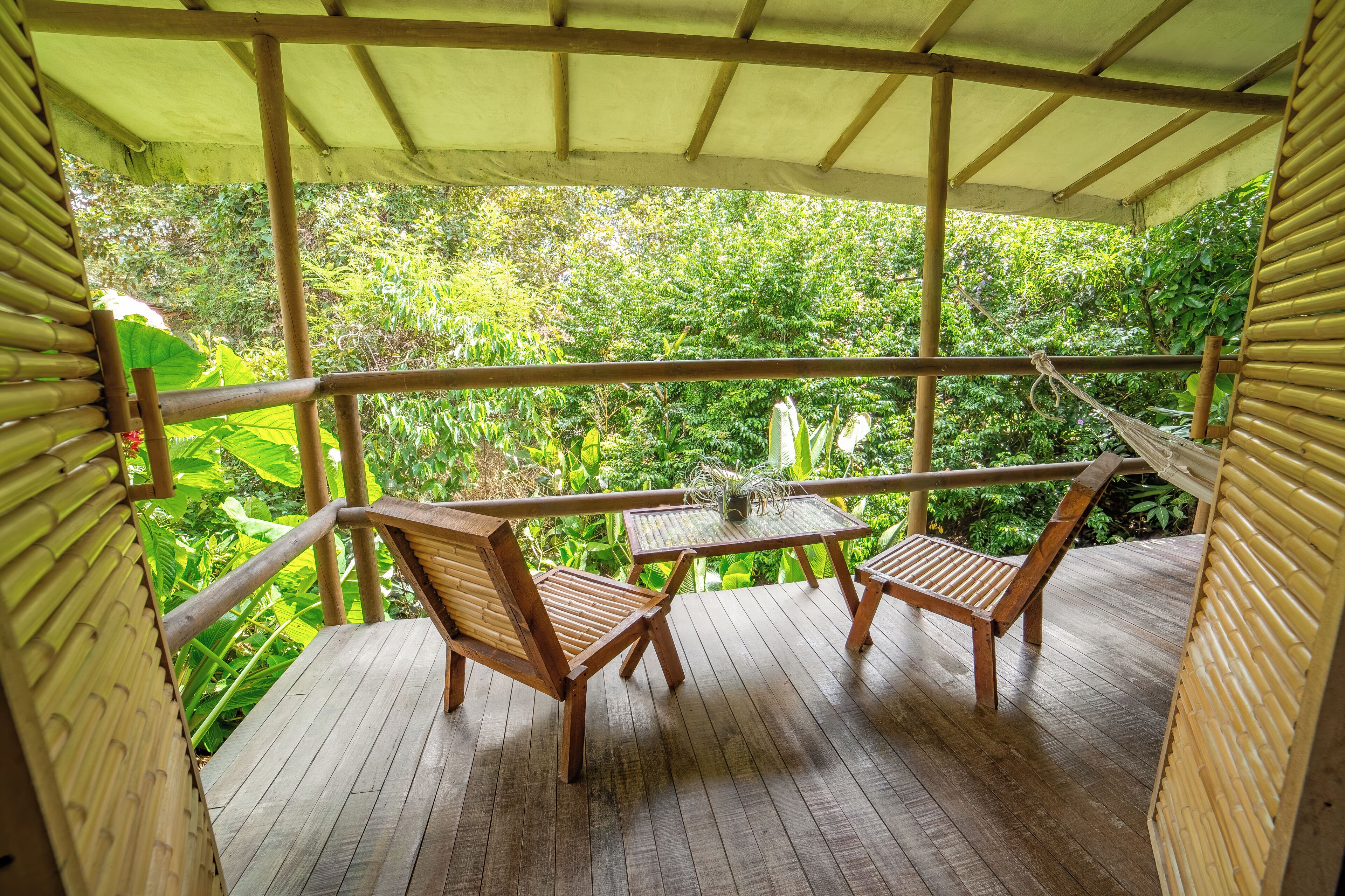 Una terraza de madera con dos sillas y una mesa, rodeada de abundante vegetación.
