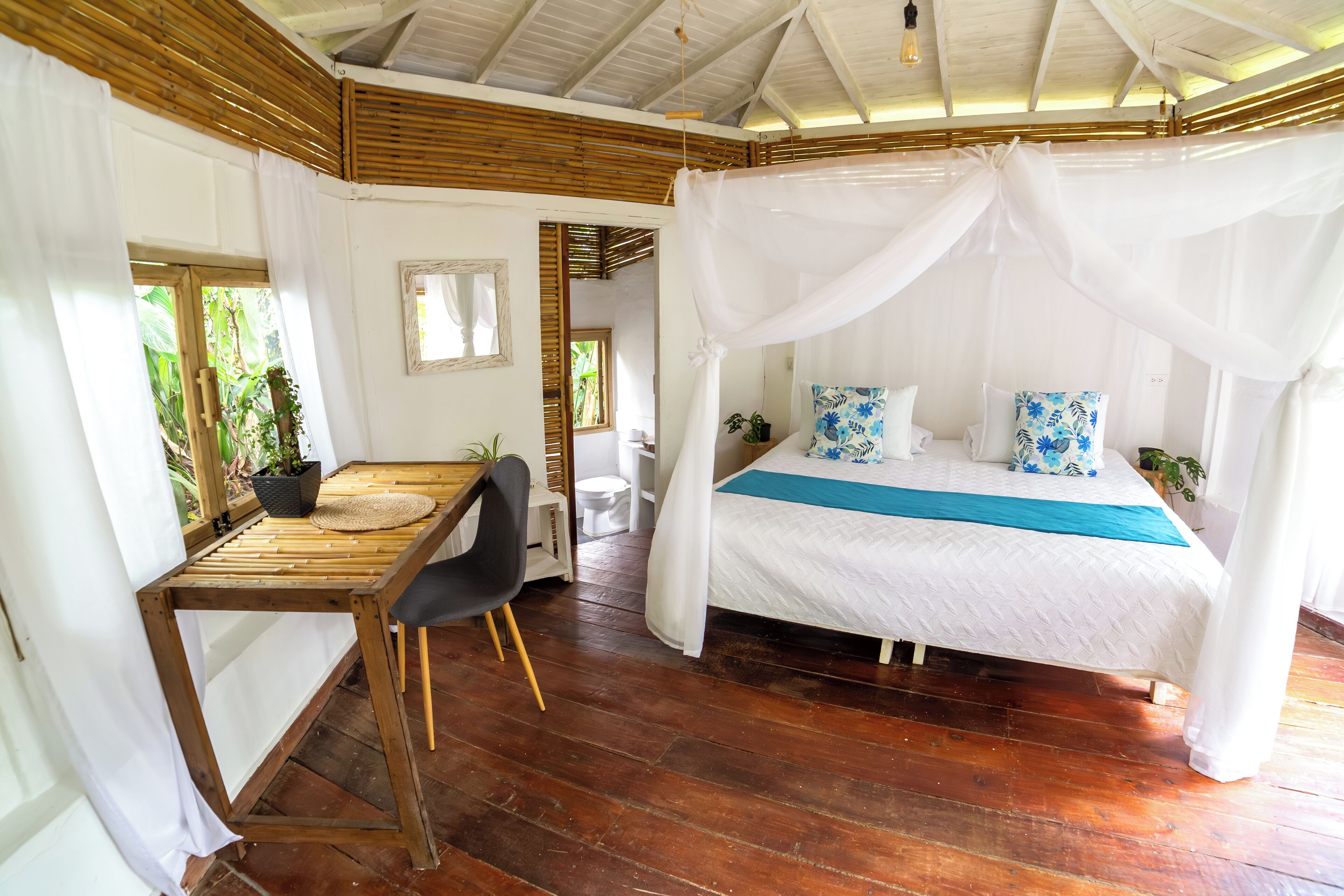Una habitación con una cama bajo un dosel, un escritorio de madera con una silla y vistas al exterior.
