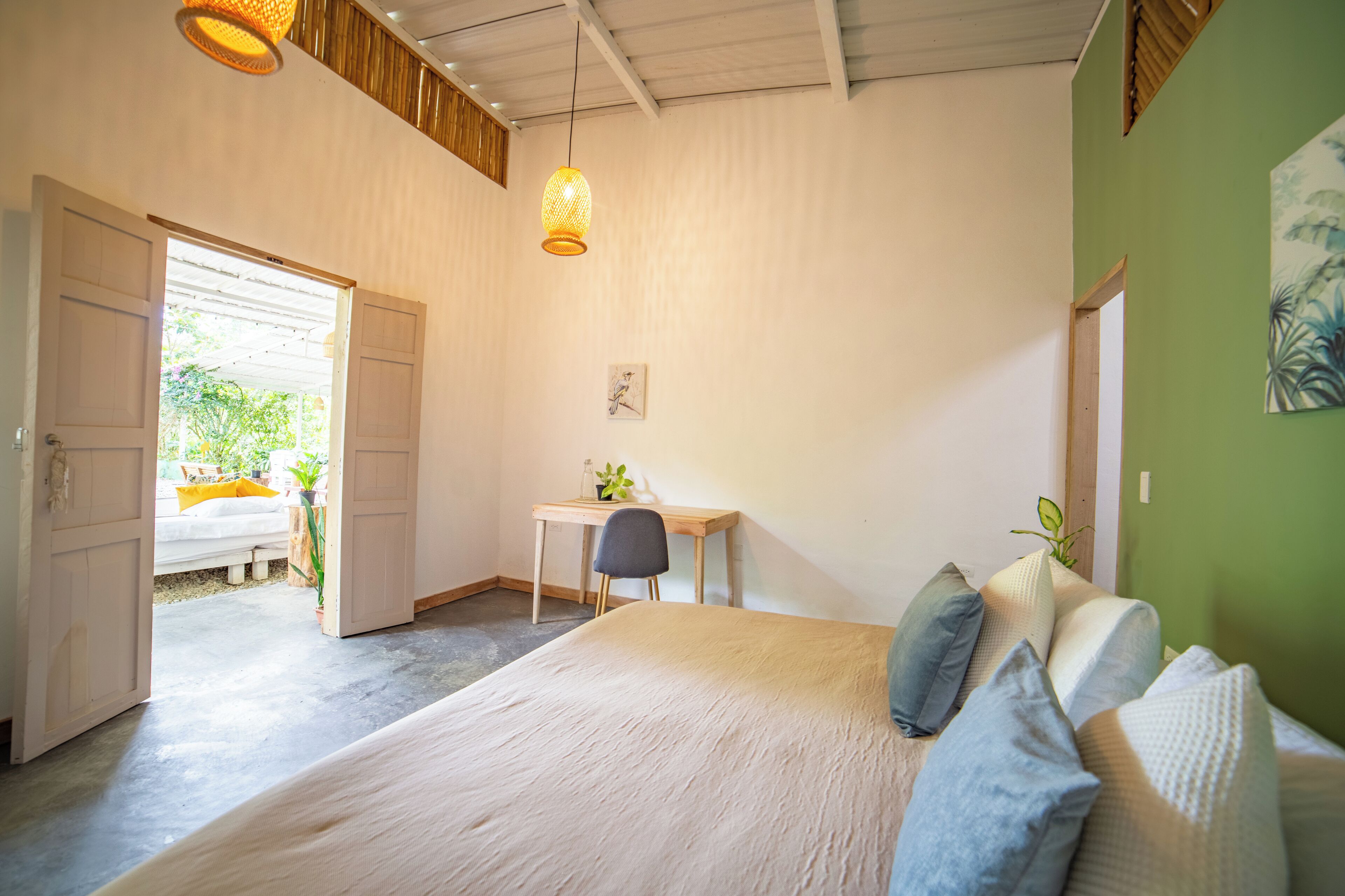 Un dormitorio con una cama, un escritorio y una silla. Hay una puerta que da a un espacio exterior.