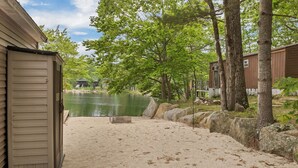 A sandy beach area with a lake view, wooden buildings, and trees. - Peak Foliage Awaits Pet-Friendly Lake Waukewan Escape Meredith NH Fall 2026 (Meredith)