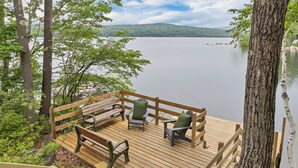 A wooden deck with benches and chairs overlooking a calm lake, surrounded by trees. - Peak Foliage Awaits Pet-Friendly Lake Waukewan Escape Meredith NH Fall 2026 (Meredith)