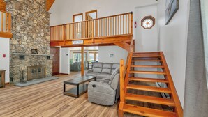 A spacious living room with a stone fireplace, a wooden staircase, and a gray sectional sofa. - Peak Foliage Awaits Pet-Friendly Lake Waukewan Escape Meredith NH Fall 2026 (Meredith)