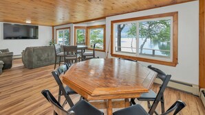 A spacious room with a large wooden dining table surrounded by chairs, large windows with a view of trees and water, and a cozy seating area with a couch and chairs. - Peak Foliage Awaits Pet-Friendly Lake Waukewan Escape Meredith NH Fall 2026 (Meredith)