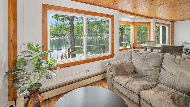 A cozy cabin interior with a large window overlooking a lake, a plush beige sofa, and a wooden ceiling. - Peak Foliage Awaits Pet-Friendly Lake Waukewan Escape Meredith NH Fall 2026 (Meredith)