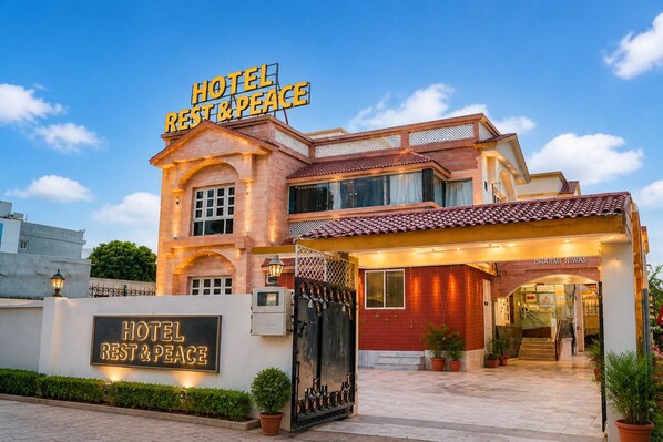 A hotel with a sign reading 'HOTEL REST & PEACE,' a gated entrance, and a visible name 'DHARMI NIWAS' on the building.