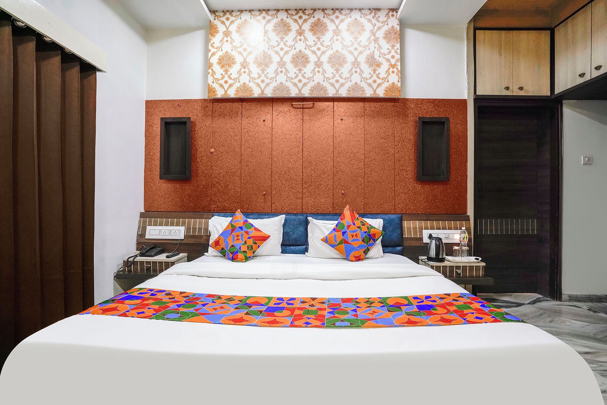 A hotel room with a large bed, two bedside tables, a wall-mounted TV, and a wardrobe.